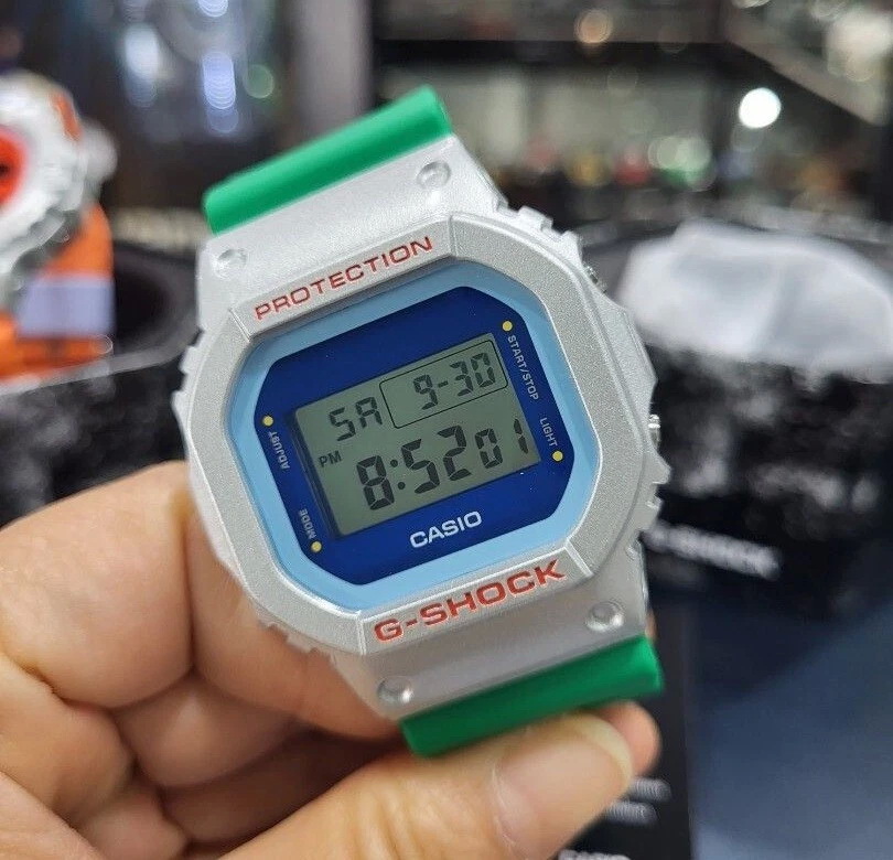 DW-5600EU-8A3D-6 ساعت مچی دیجیتال مردانه Casio G‑SHOCK DW‑5600EU‑8A3D با قاب طوسی روشن مات، بند رزین روشن، طراحی مربعی کلاسیک، مقاومت ضربه، نور پسزمینه EL و مقاومت آب ۲۰۰ متر مناسب استفاده روزمره و اسپرت